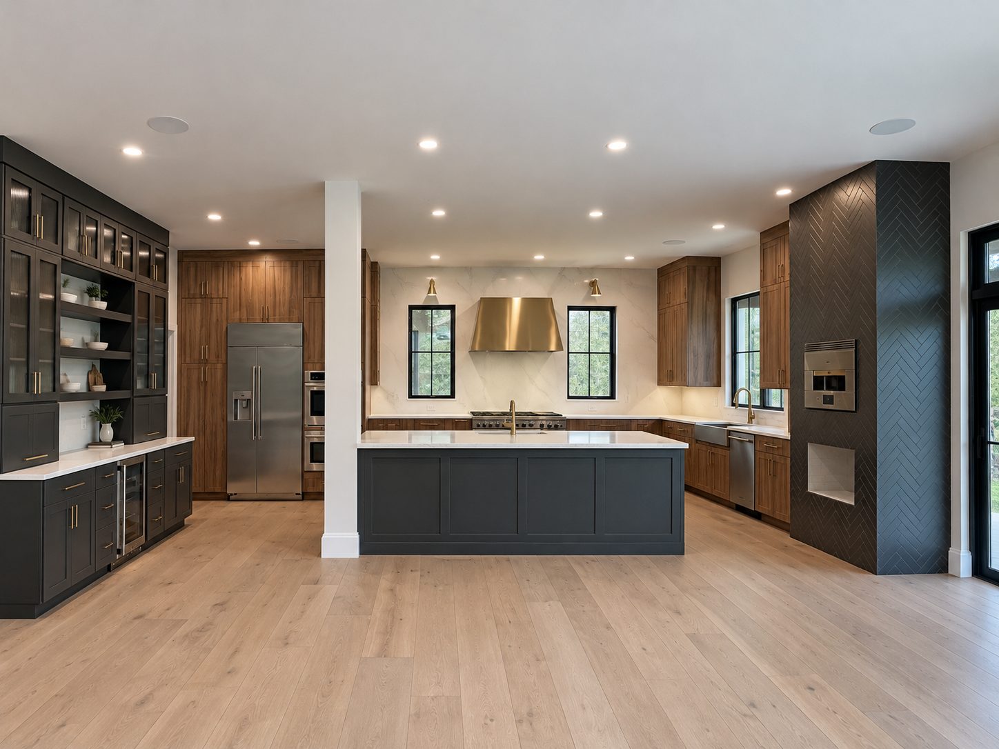 Open kitchen with walnut cabinetry, charcoal island, brass range hood, built-in glass-front cabinets and a black herringbone-tile column