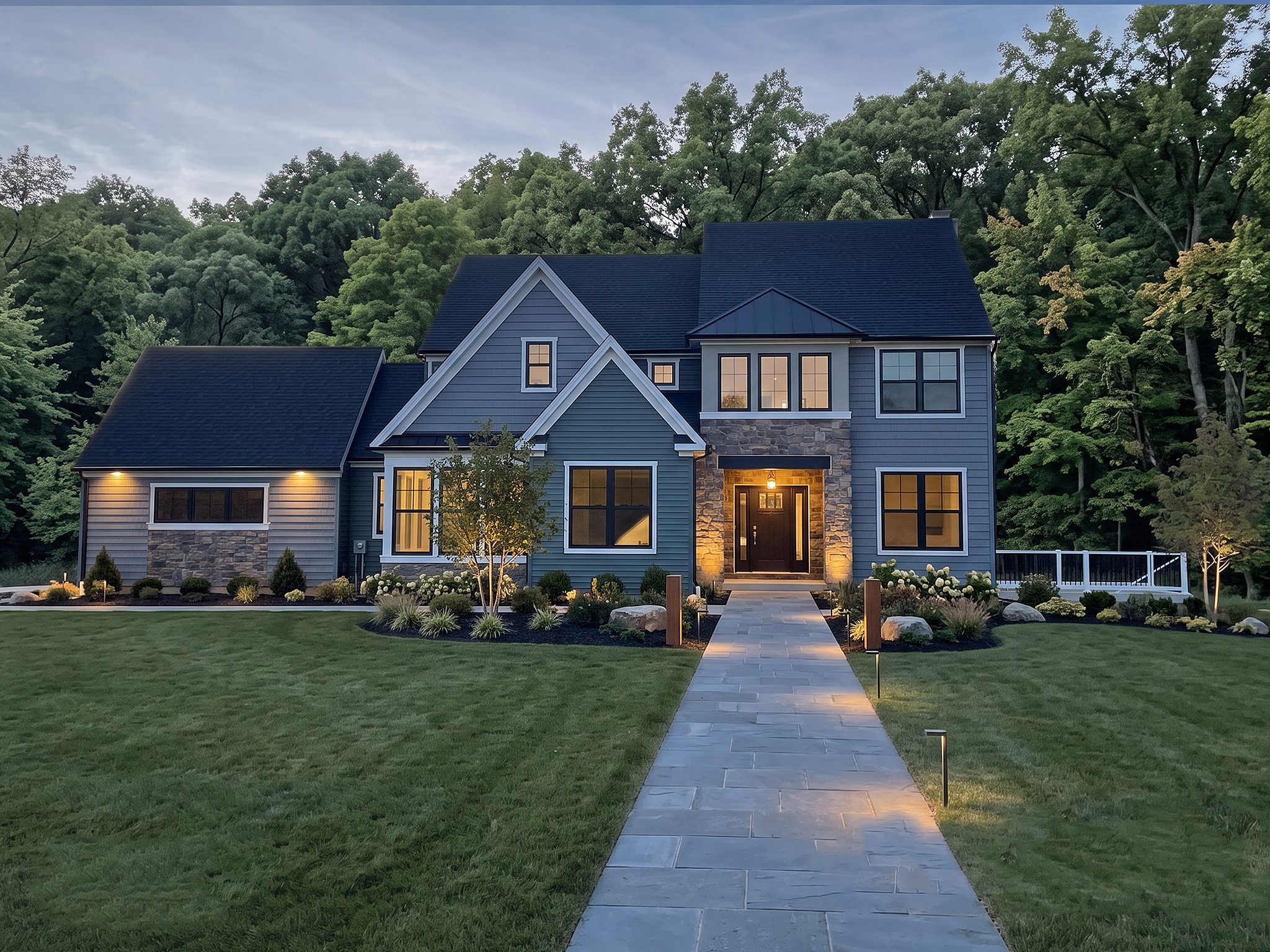 Two-story home with blue-gray siding and stone entry, lit at dusk with a bluestone walkway