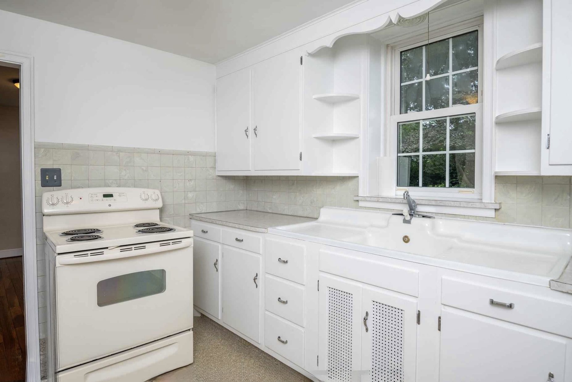 Before: white kitchen with a coil range and a farmhouse sink under the window