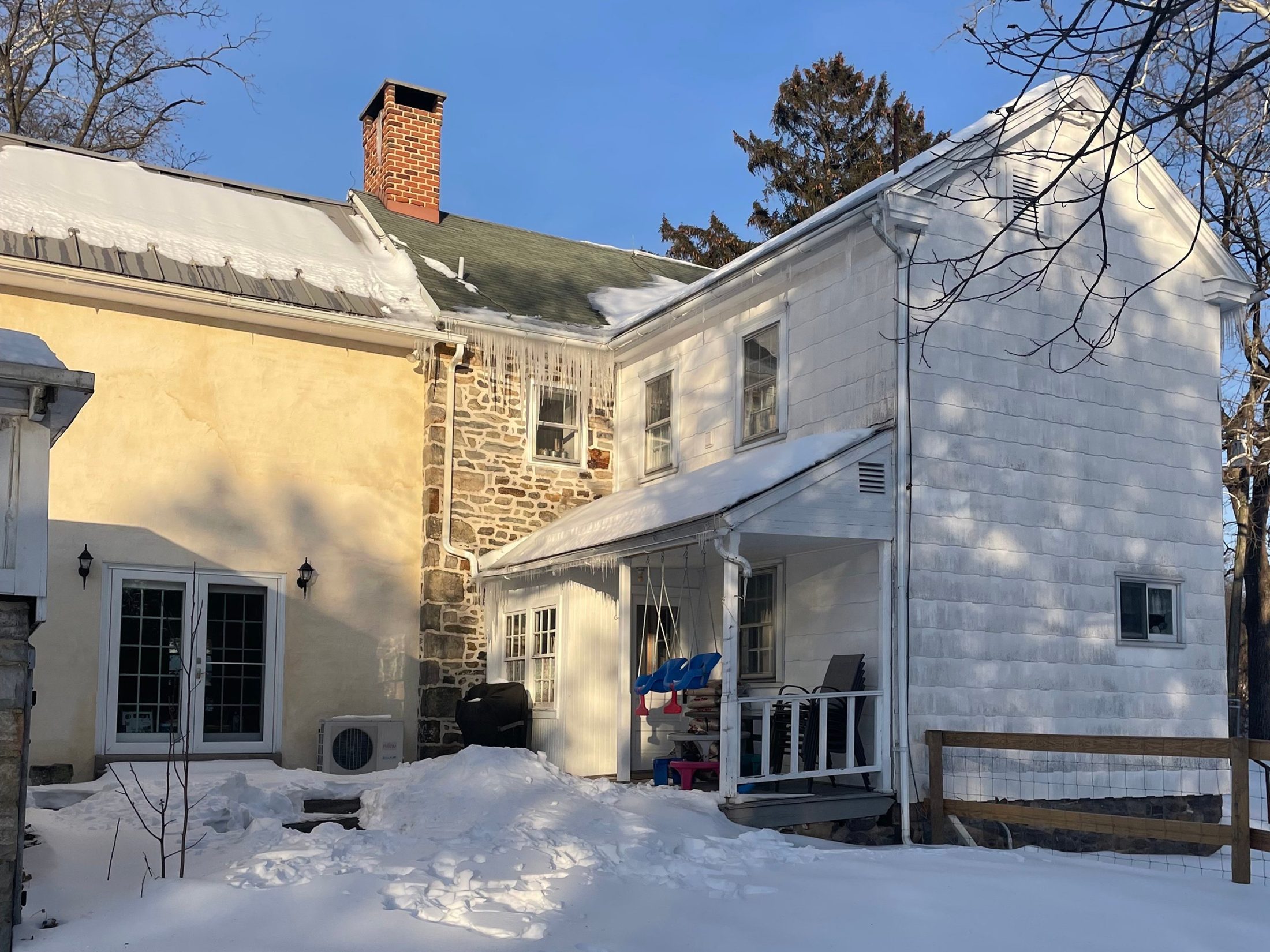 The rear of the stone farmhouse before the addition, in snow, with yellow stucco wing and a small covered porch