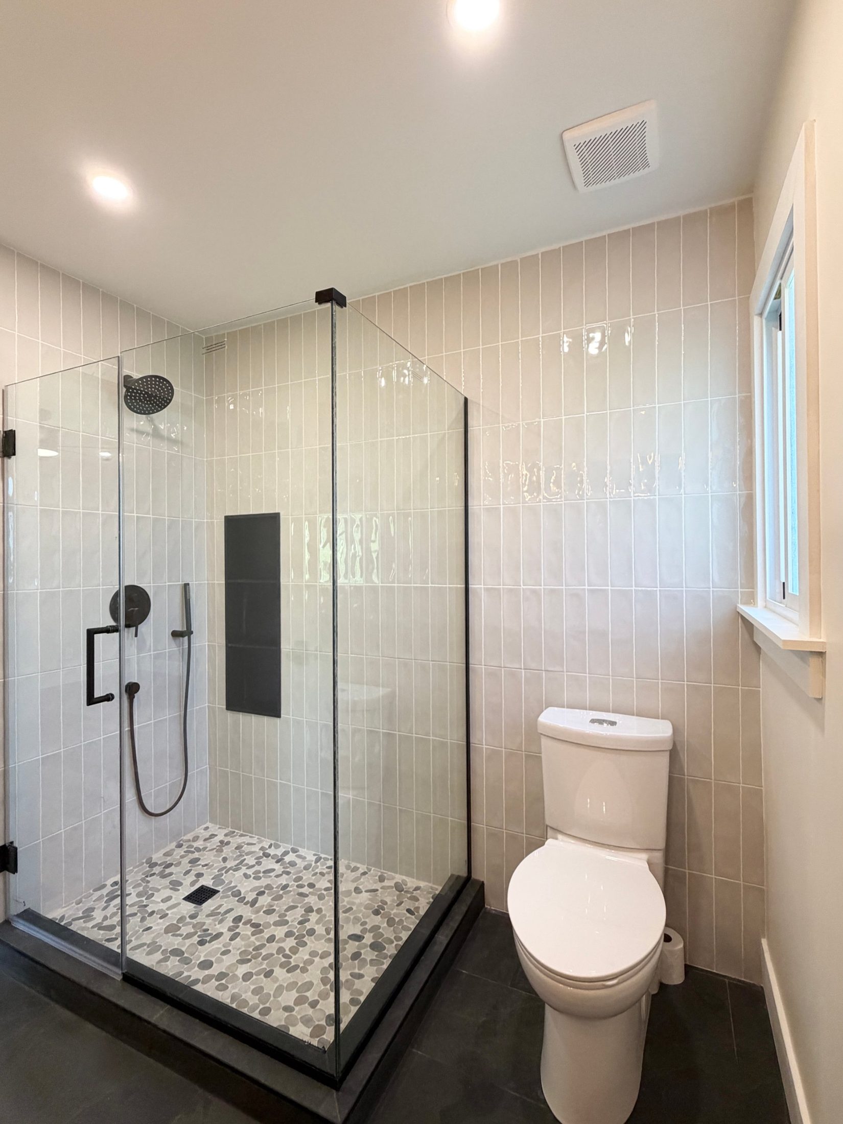 Finished primary bath with a frameless glass shower, vertical glazed tile, black fixtures and a niche