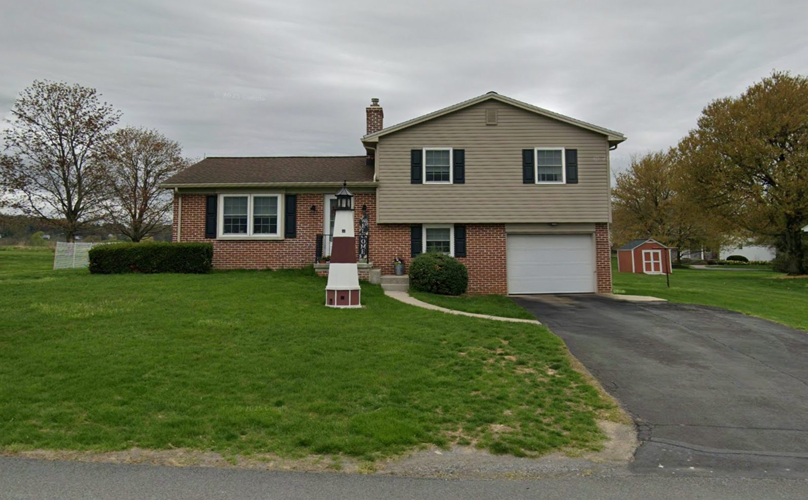 The same split-level home before: tan vinyl siding, brick and a single-car garage