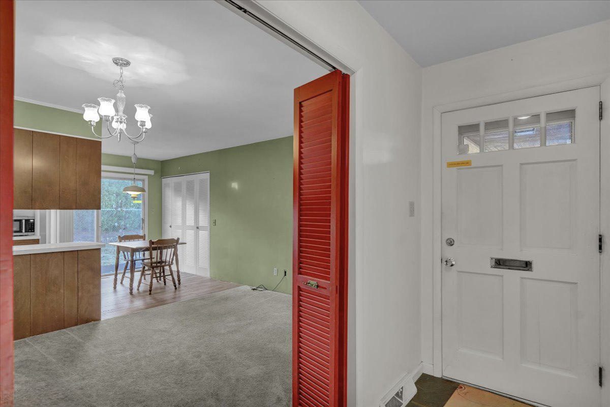 Before: the entry and dining area with a white paneled front door, red louvered closet door and gray carpet