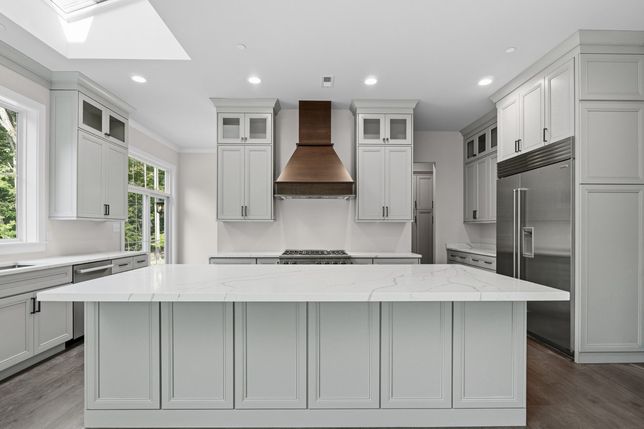 Kitchen with pale gray inset cabinets, a large quartz island, a copper range hood and a built-in stainless refrigerator