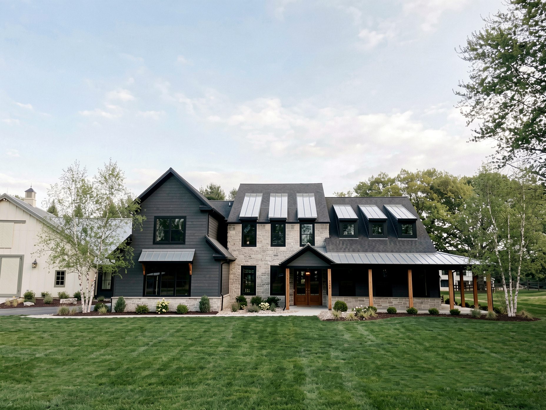 Two-story home with charcoal siding, stone, standing-seam metal roof and a wraparound porch with cedar posts
