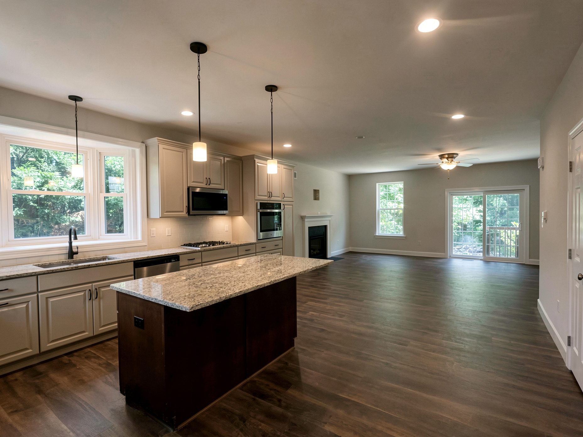Open kitchen with granite-topped island, pendant lights and a bay window, flowing into a living area with a gas fireplace and sliding doors